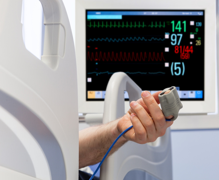 Patient's Hand in Bed with Oximeter and Monitor on Background