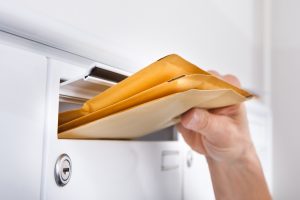 Close-up Of Postman Putting Letters In Mailbox