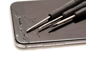 Broken smartphone and small screwdrivers for repair on white background